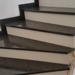 Szczegółowe ujęcie schodów z ciemnego kamienia z jasnymi podstopnicami, widoczne fragmenty ściany z drobnymi uszkodzeniami.