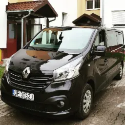 Czarny bus Renault Trafic z tablicą rejestracyjną z Opola, zaparkowany przed budynkiem mieszkalnym.