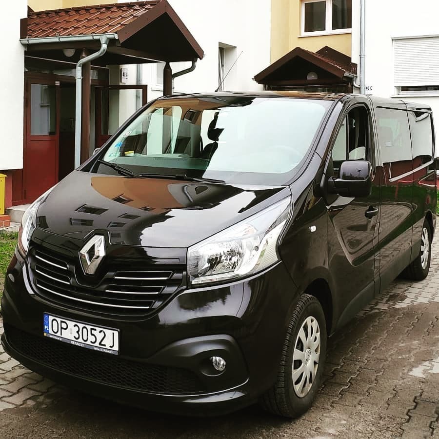 Czarny bus Renault Trafic z tablicą rejestracyjną z Opola, zaparkowany przed budynkiem mieszkalnym.