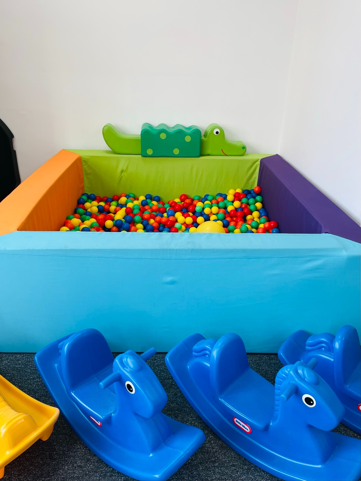 Kącik zabaw dla dzieci z basenem z kolorowymi piłeczkami, pluszowym krokodylem i niebieskimi konikami na biegunach Little Tikes.