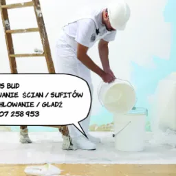 Malarz w białym kombinezonie i kasku przelewa farbę z jednego wiadra do drugiego, drabina oparta o ścianę, zabezpieczona folią kanapa w tle, podłoga pokryta folią ochronną.