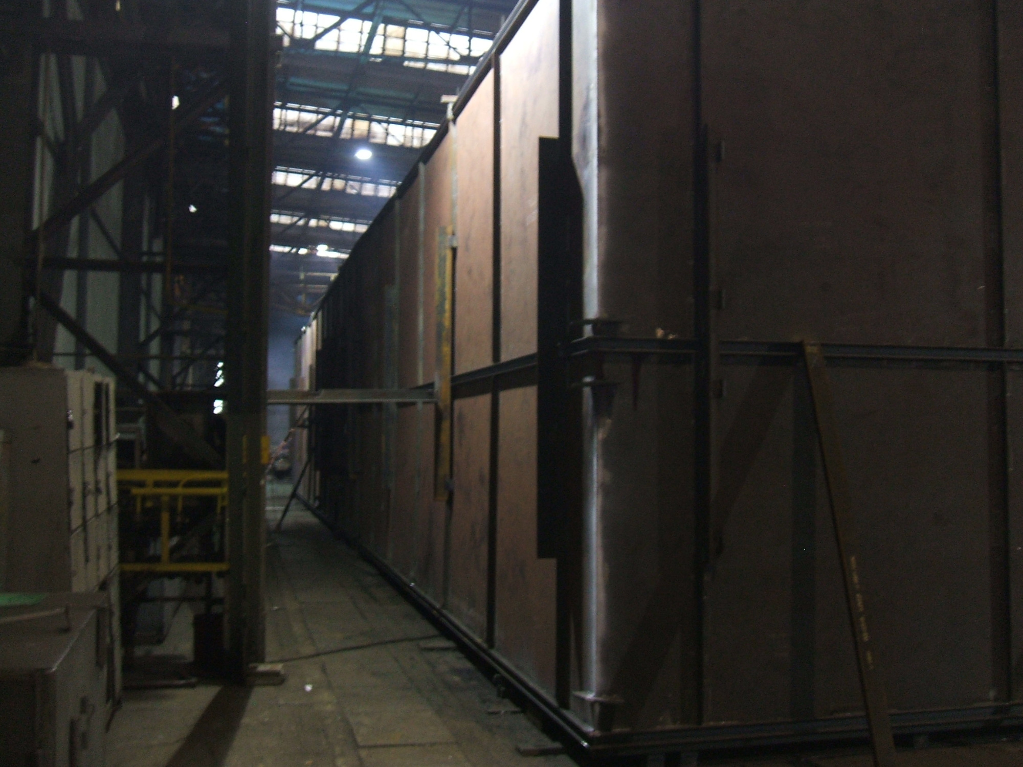 Wnętrze hali produkcyjnej z długim, metalowym korytarzem i konstrukcją wsporczą pod sufitem.