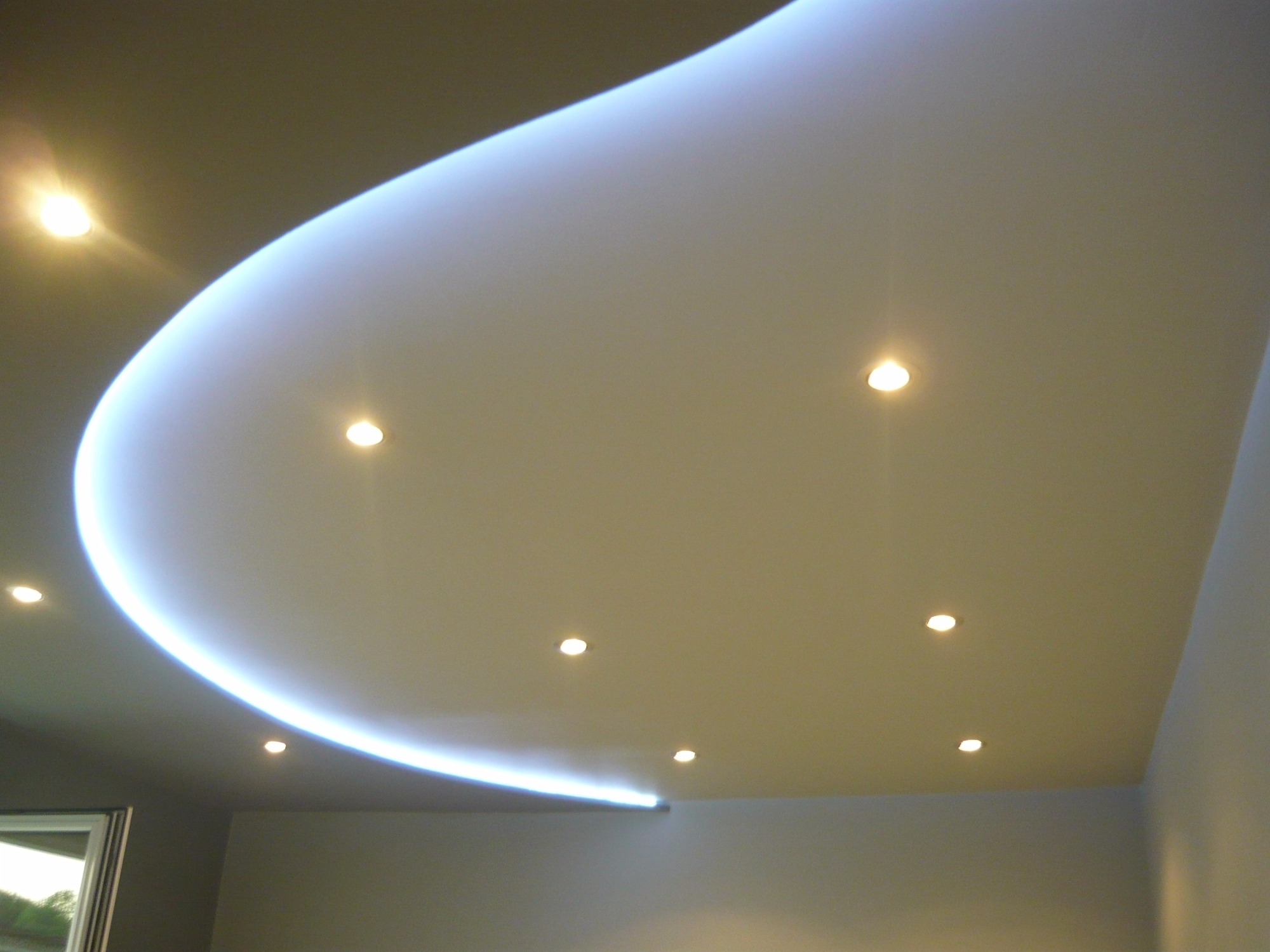 Nowoczesny, podwieszany sufit z oświetleniem LED w kształcie łuku i punktowymi lampami halogenowymi, widok z dołu.