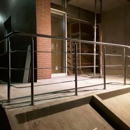 WELDER-SERWIS OLGA SIWIK - Zewnętrzna barierka ze stali nierdzewnej z poziomymi prętami, zamontowana na betonowym podeście schodów, z widocznym rusztowaniem w tle i osobą pracującą przy oświetleniu.