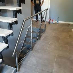 WELDER-SERWIS OLGA SIWIK - Wnętrze z nowoczesnymi schodami o konstrukcji stalowej i drewnianych stopniach zabezpieczonymi metalową, minimalistyczną, chromowaną barierką, w tle widoczny pracownik w kombinezonie i niedbale...