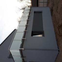 WELDER-SERWIS OLGA SIWIK - Nowoczesny budynek z szarą elewacją i balkonem z szkła i metalu, widok z dołu, surowy teren wokół budynku.