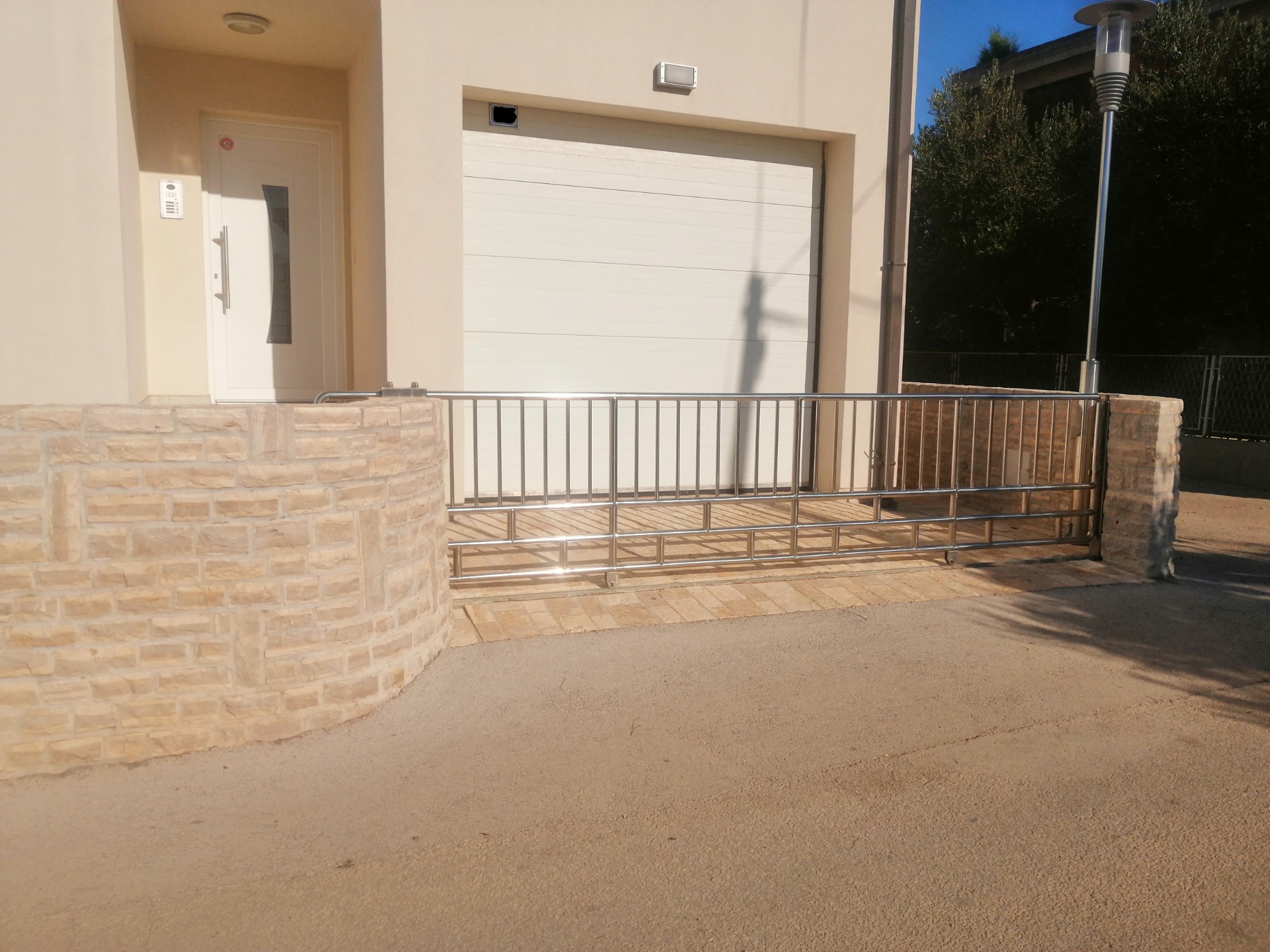 Nowoczesna barierka ze stali nierdzewnej przed budynkiem z garażem, zamontowana na niskim murku z piaskowca.