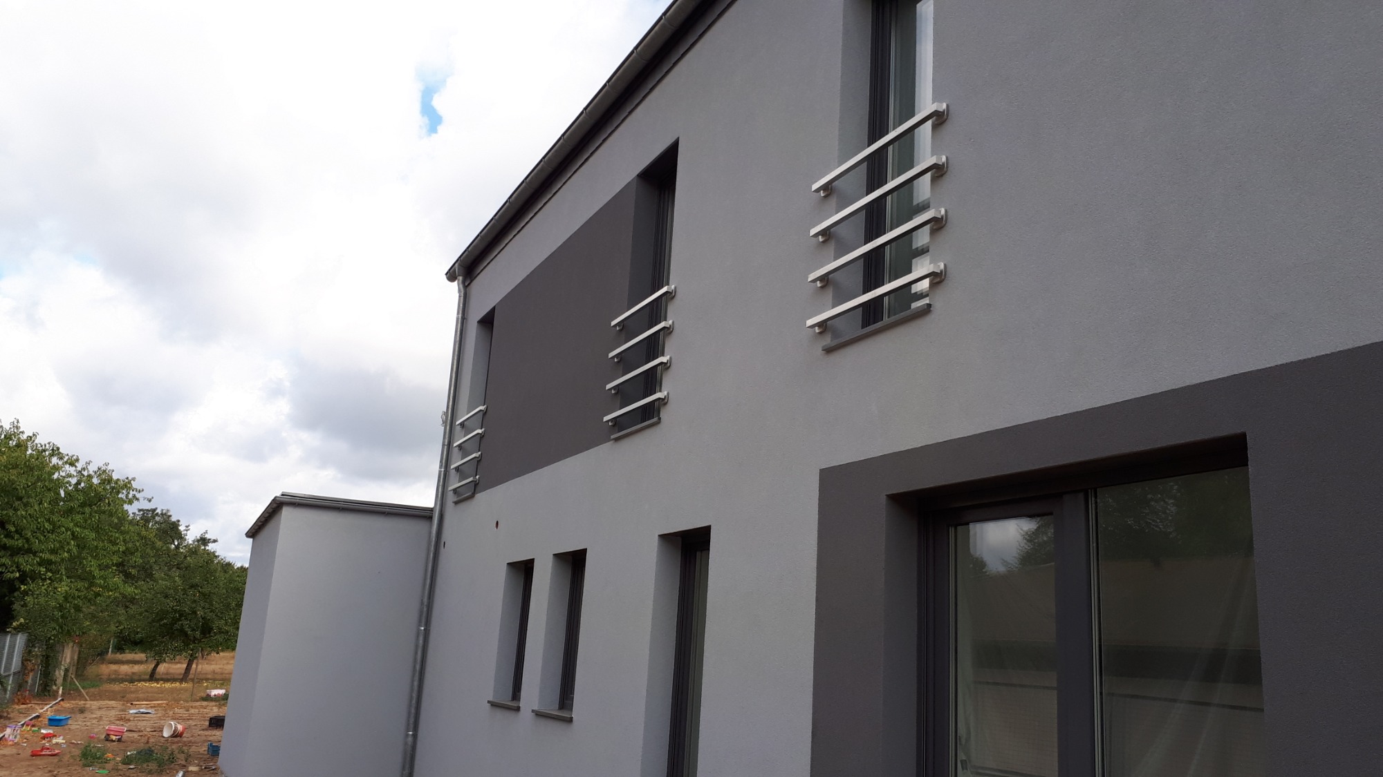 Nowoczesny dom dwukondygnacyjny z szarą elewacją i oknami zabezpieczonymi prostymi, poziomymi barierkami ze stali nierdzewnej.