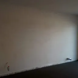 Świeżo otynkowane ściany w jasnym pomieszczeniu z widocznymi instalacjami elektrycznymi i hydraulicznymi przed wykończeniem.