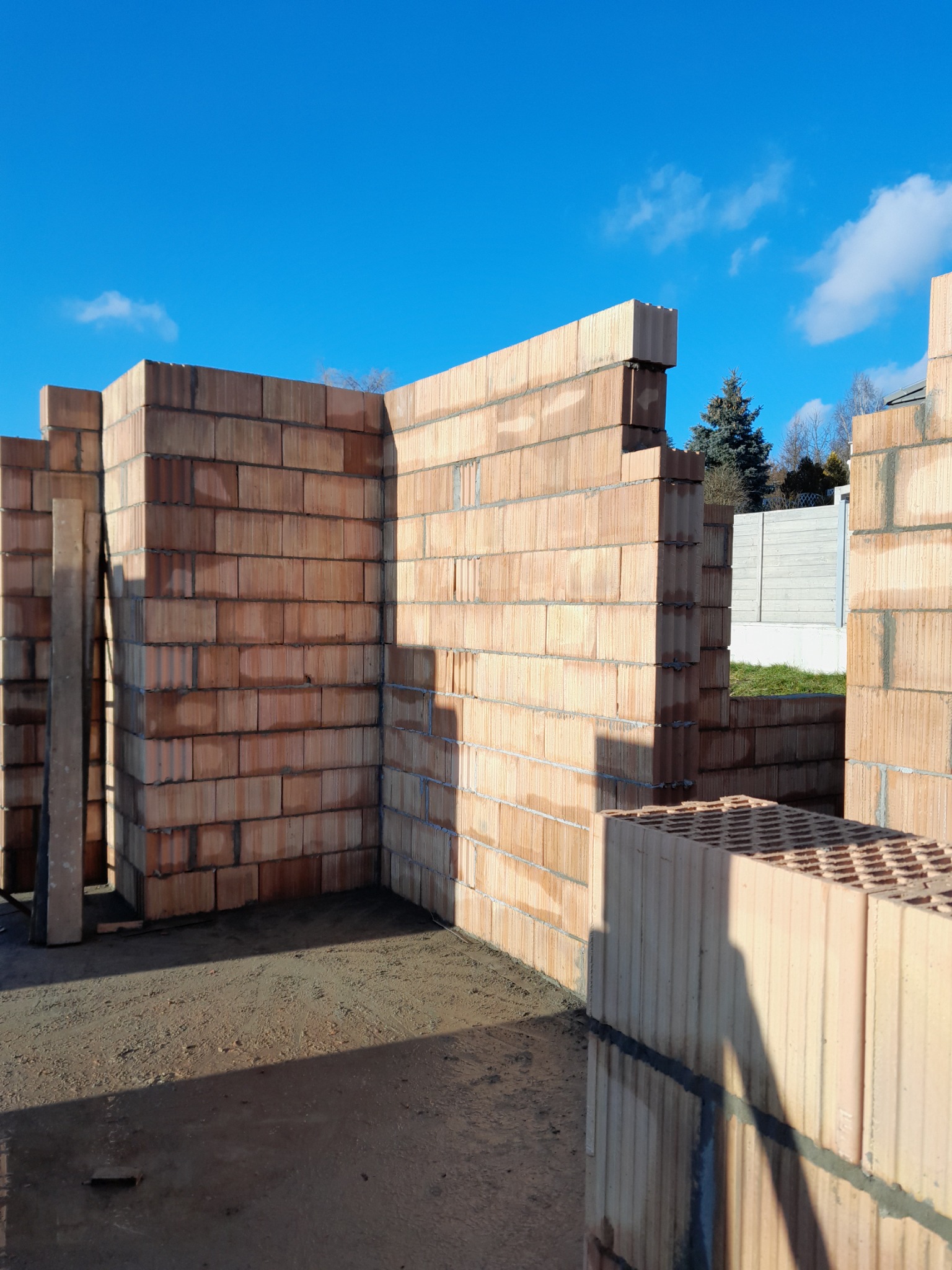 Wznoszone ściany z pustaków ceramicznych na fundamencie, widoczne spoiny i niebo w tle.