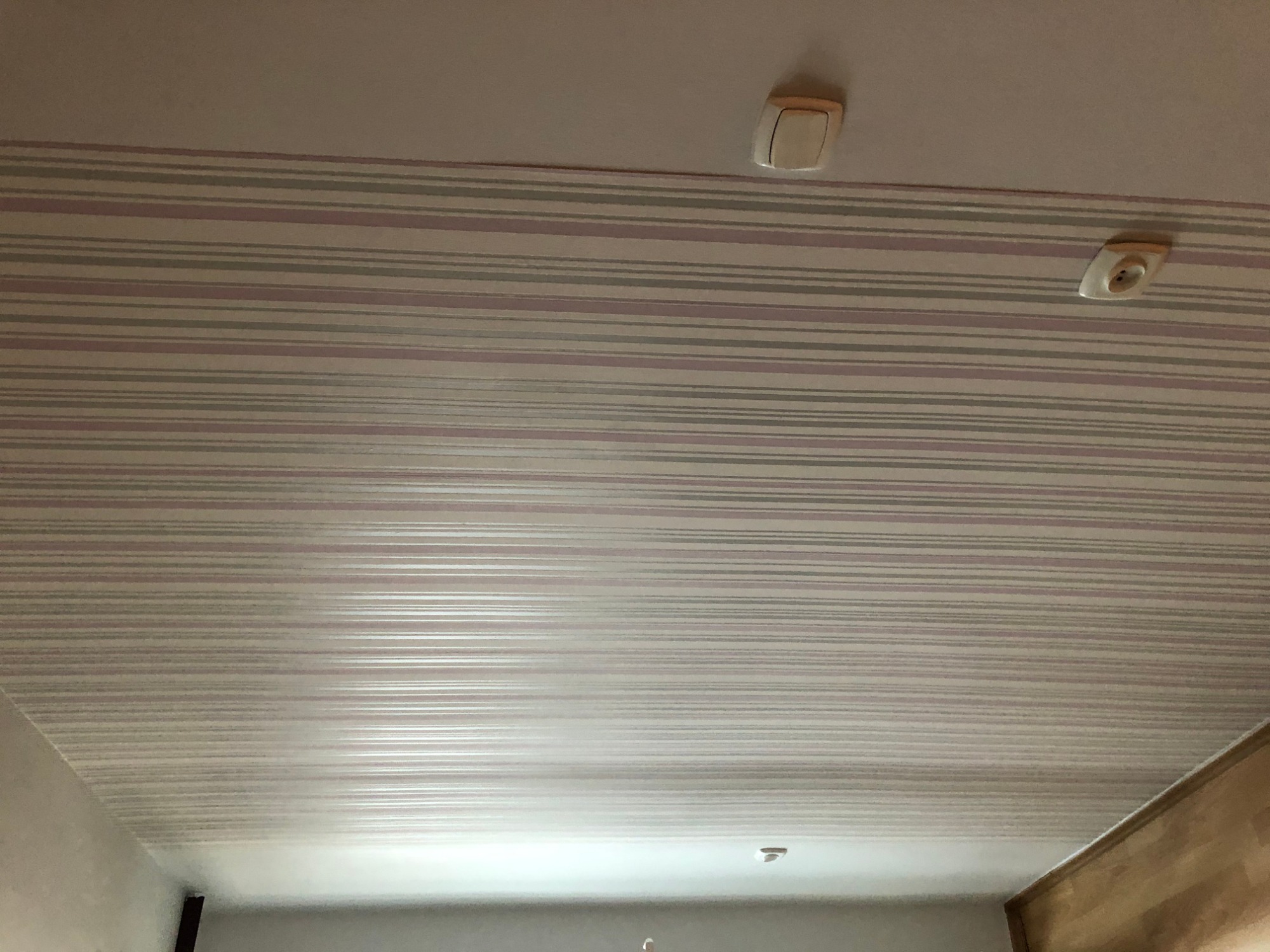Paski tapety na suficie z widocznym gniazdkiem elektrycznym i włącznikiem światła.