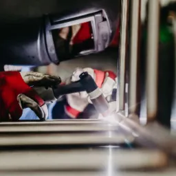 Spawanie ramy z metalowych rurek przez spawacza w masce ochronnej i rękawicach roboczych, widoczny błysk spawu.