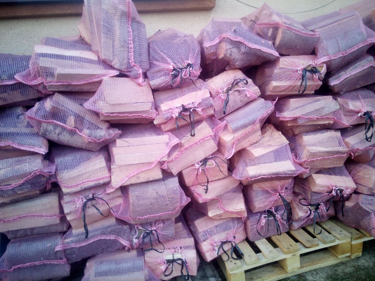 Stos worków z pociętym drewnem ułożonych na palecie, zabezpieczonych różową siatką.