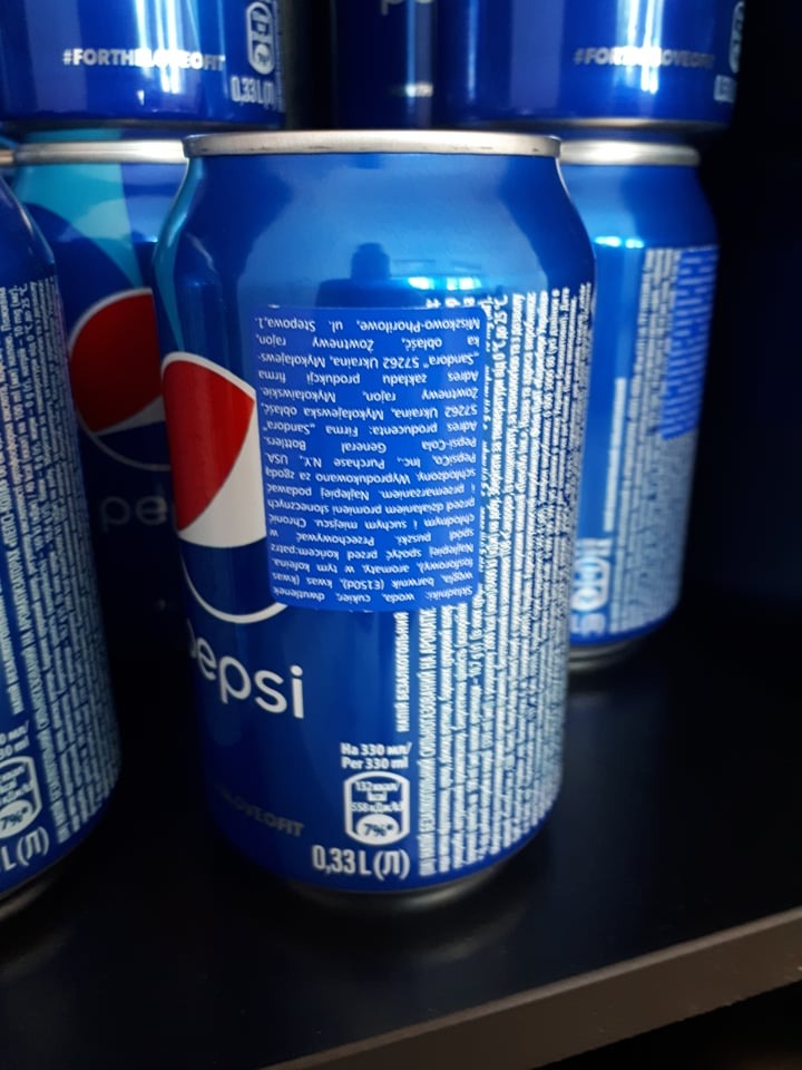 Metalowe puszki z napojem gazowanym Pepsi, ustawione jedna za drugą, z widocznymi etykietami z informacjami o składzie w języku ukraińskim, oświetlone z góry.
