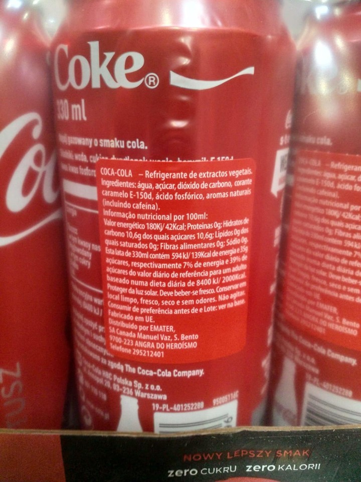 Szczegółowe ujęcie kilku czerwonych puszek napoju gazowanego z widocznym składem i wartościami odżywczymi, z etykietą 'Nowy lepszy smak zero cukru zero kalorii'.