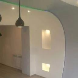 Nowoczesne wnętrze z zaokrągloną ścianą w odcieniach szarości, wnękami oświetleniowymi i designerskimi lampami wiszącymi w kształcie kropli, drewniana podłoga.