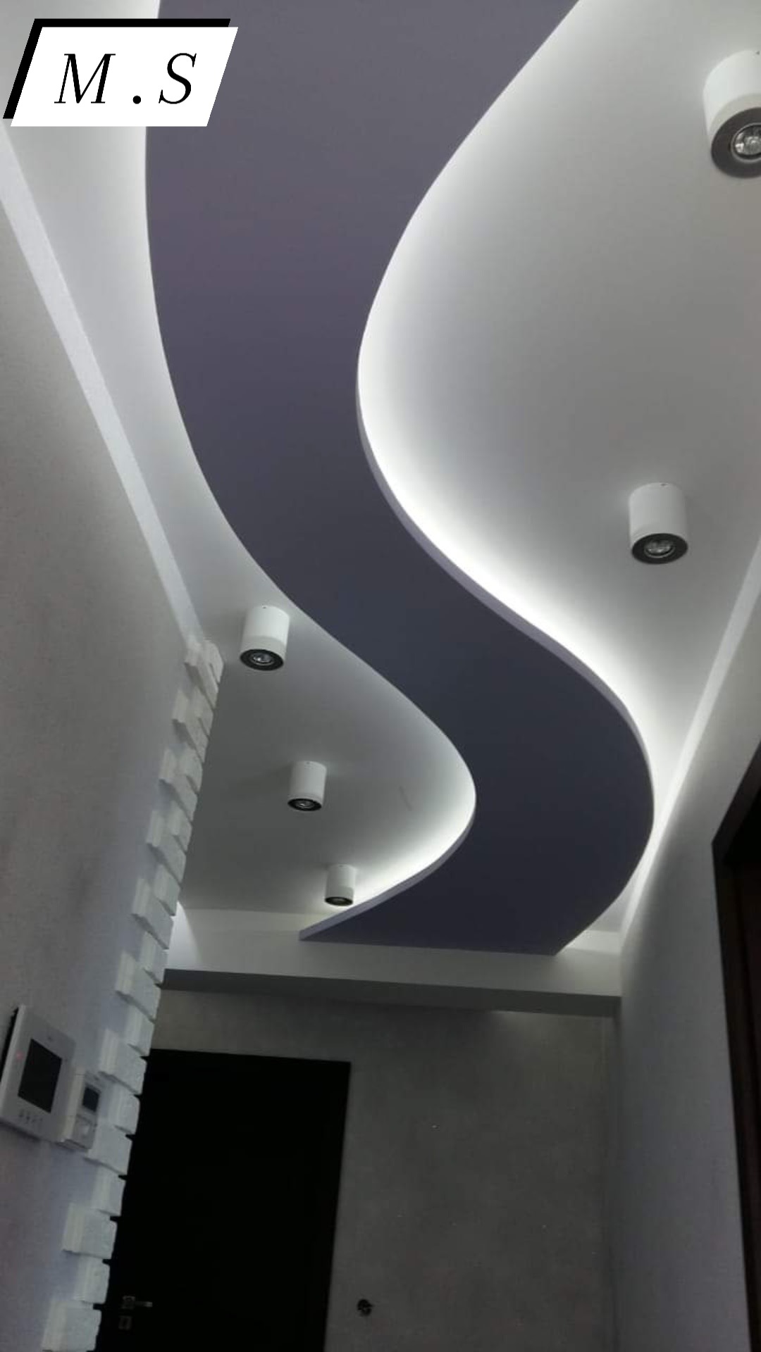 Sufit z płyt karton gips z podświetleniem LED w kształcie litery S, oświetlenie punktowe, dekoracyjna ściana z białych elementów, widok z dołu.