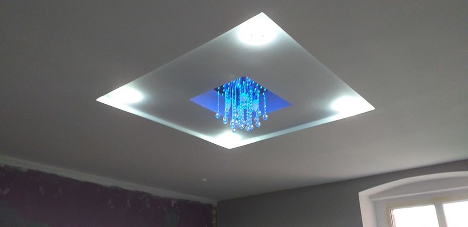 Podwieszany sufit z oświetleniem punktowym i dekoracyjnym żyrandolem w Lwówku Śląskim, z nieukończonymi pracami malarskimi na ścianach.