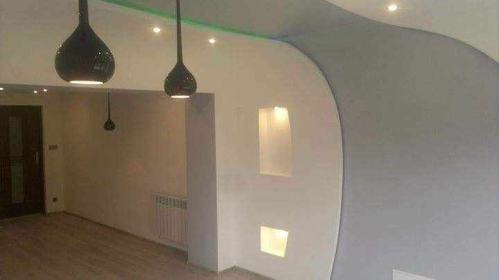 Nowoczesne wnętrze z zaokrągloną ścianą w odcieniach szarości, wnękami oświetleniowymi i designerskimi lampami wiszącymi w kształcie kropli, drewniana podłoga.