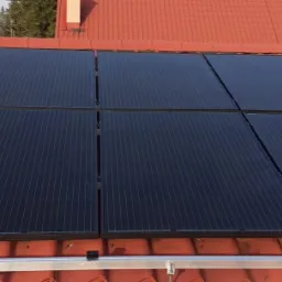 Panele słoneczne zamontowane na czerwonym, ceramicznym dachu domu jednorodzinnego, widoczne elementy montażowe.