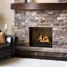 Murowany element grzewczy z kamienia w salonie, z paleniskiem i dekoracyjną drewnianą półką nad nim. Obok stoi skórzany fotel i świeca.