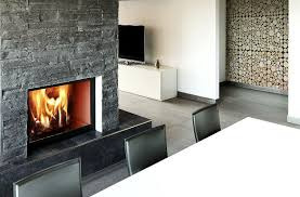 Nowoczesny salon z wbudowanym paleniskiem obudowanym szarą, kamienną okładziną. W tle widoczna ściana dekoracyjna z ułożonych plastrów drewna i minimalistyczne meble.