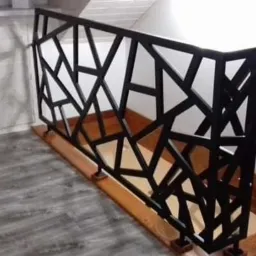 Czarna, metalowa balustrada schodowa o geometrycznym wzorze w nowoczesnym wnętrzu z szarymi panelami podłogowymi.