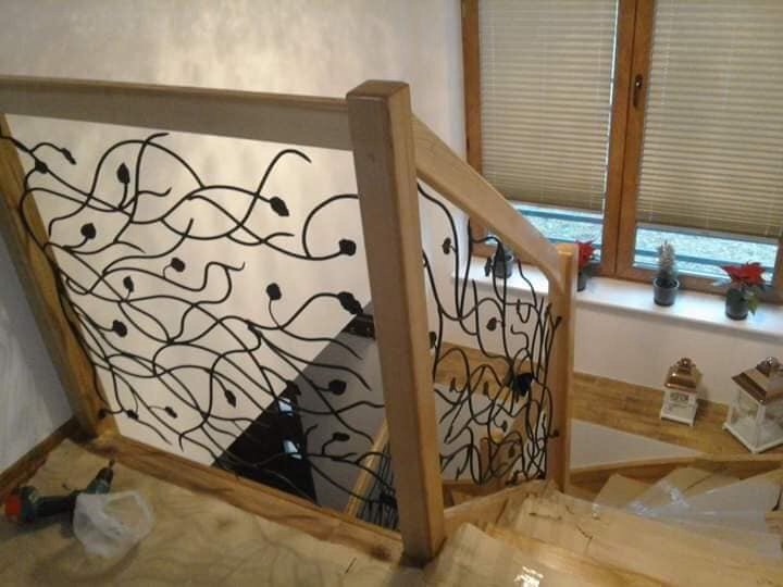 Drewniana balustrada schodowa z dekoracyjnym, metalowym wypełnieniem o motywie roślinnym, widok z góry na schody w trakcie montażu, narzędzia pracy obok.