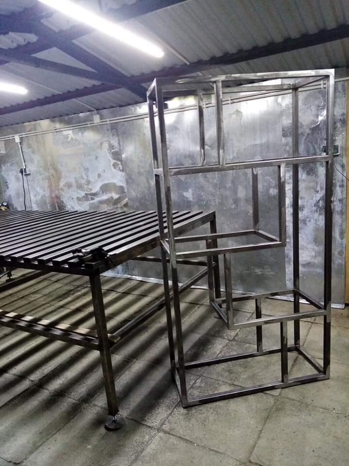 Spawana konstrukcja metalowa regału i stołu warsztatowego w surowym wnętrzu hali.