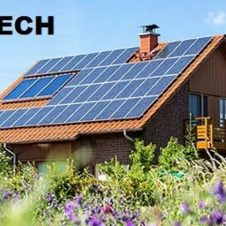 Dom jednorodzinny z panelami słonecznymi na dachu, widok z poziomu ogrodu z kwitnącymi kwiatami, logo firmy w lewym górnym rogu.