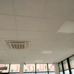 Kasetonowy sufit podwieszany w biurze z wbudowaną klimatyzacją, widok z dołu na białe panele i kratki wentylacyjne.