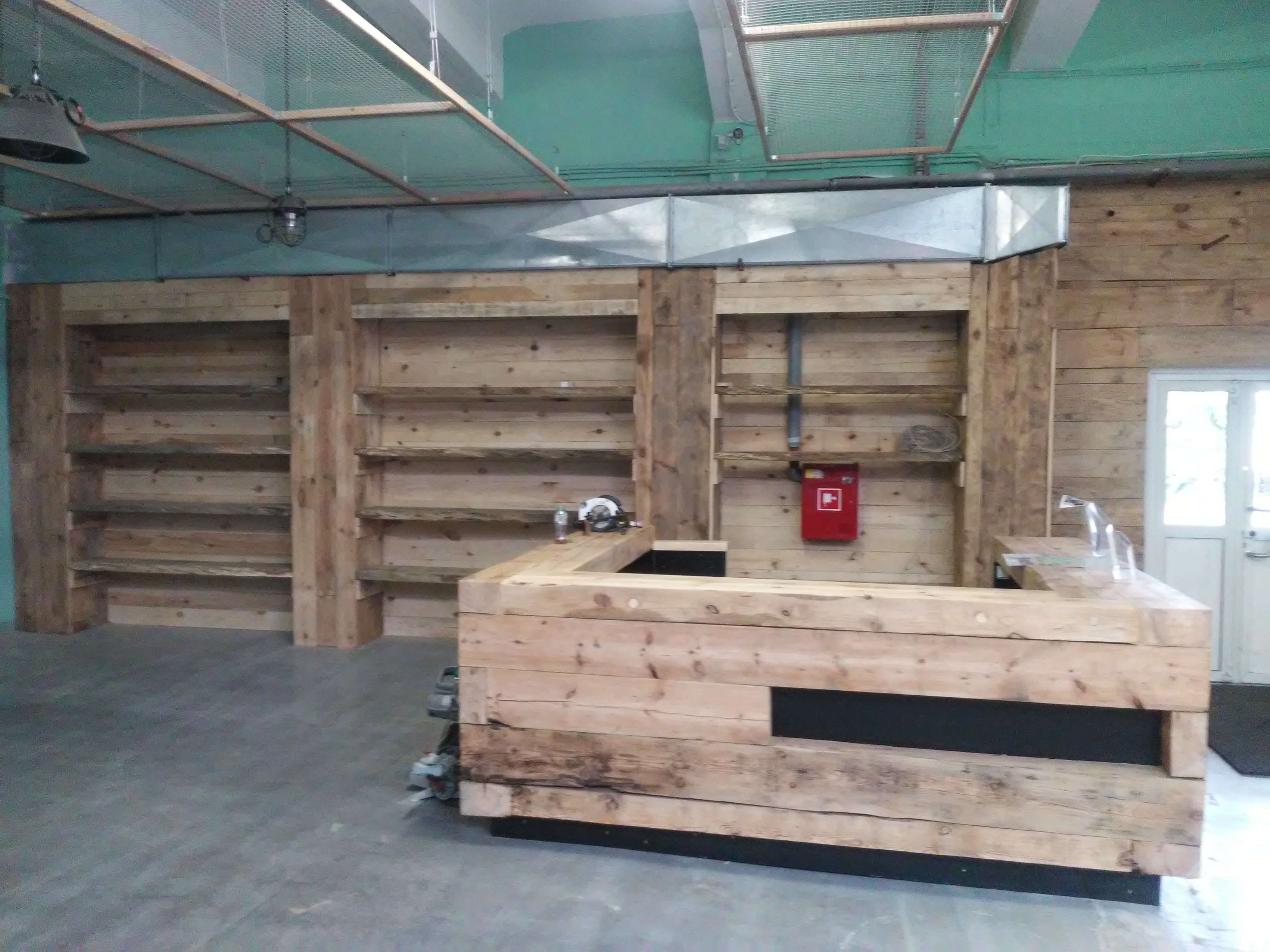 Wykończone wnętrze biura z drewnianą ladą recepcyjną i regałami z surowego drewna, widoczny fragment sufitu z instalacjami.