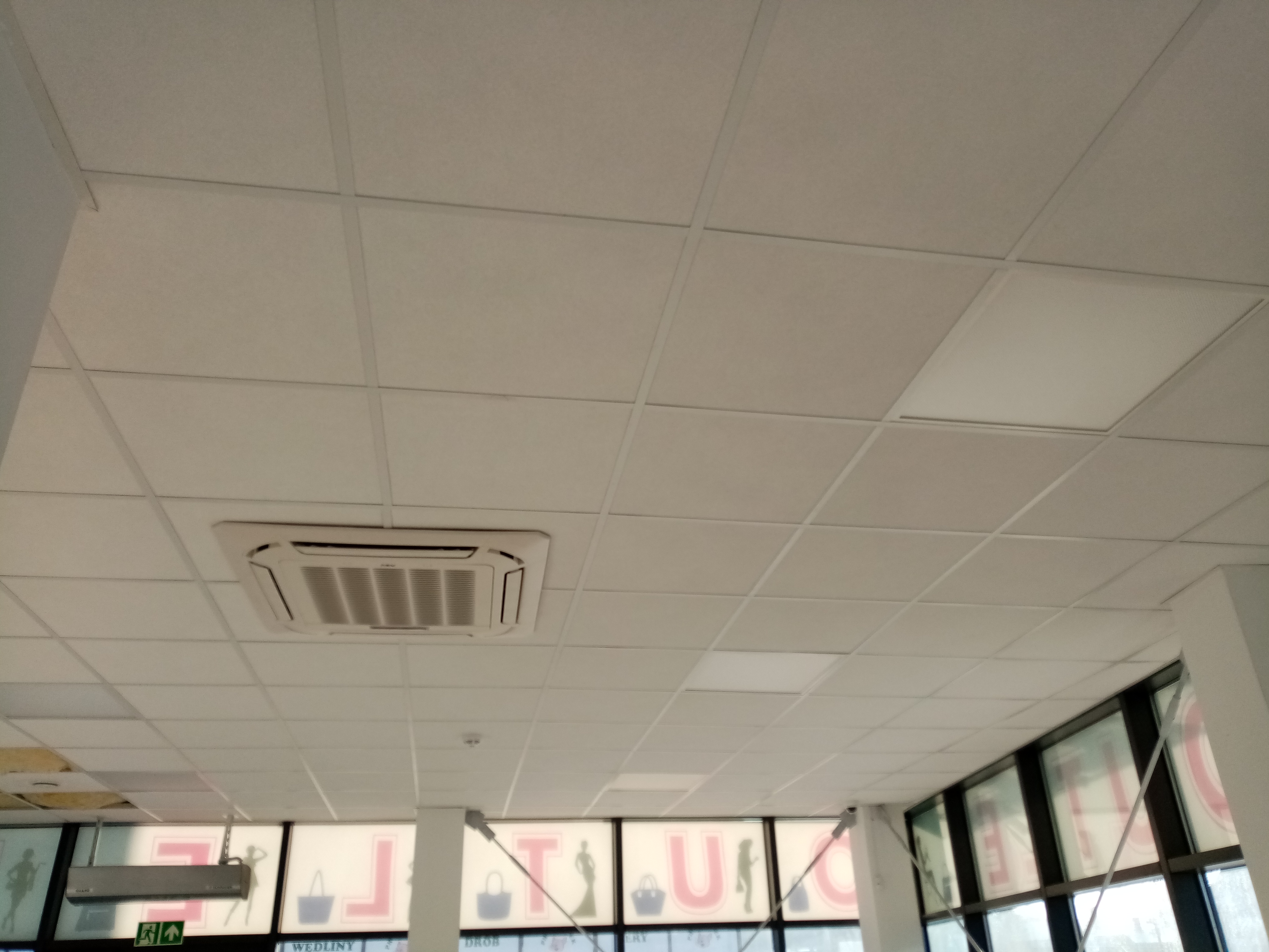 Kasetonowy sufit podwieszany w biurze z wbudowaną klimatyzacją, widok z dołu na białe panele i kratki wentylacyjne.