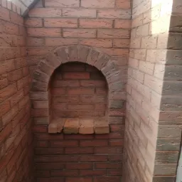 Wnęka z łukiem wykończona czerwoną cegłą klinkierową, z widoczną strukturą i fugami, w narożniku pomieszczenia oświetlonego z prawej strony.