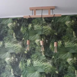 Lampa wisząca z trzema żarówkami Edisona na tle tapety z motywem tropikalnych liści palmy.