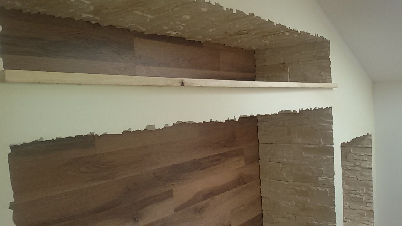 Wnęka w ścianie z okładziną z paneli drewnopodobnych i kamienia dekoracyjnego, półka z surowego drewna, widoczne nierówne krawędzie łączenia materiałów.