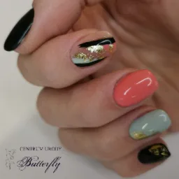 Dłoń z asymetrycznym manicure: czarny, koralowy i miętowy lakier z elementami złota.