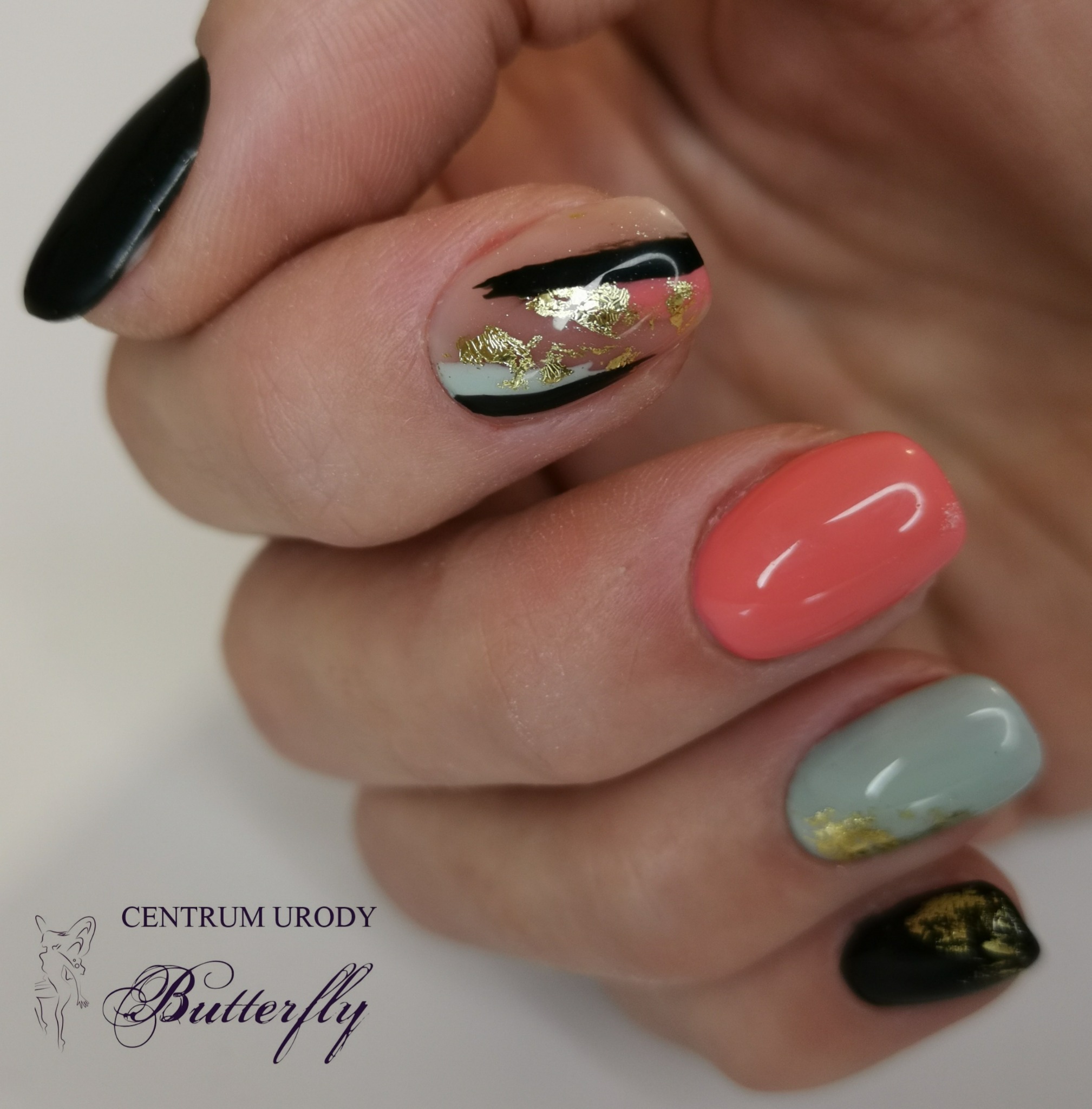Dłoń z asymetrycznym manicure: czarny, koralowy i miętowy lakier z elementami złota.
