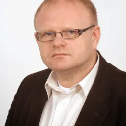 Portret mężczyzny w okularach i brązowym sztruksowym marynarce na białym tle.