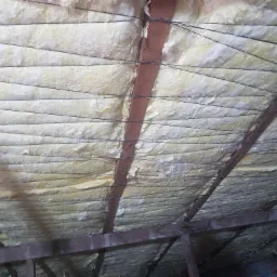 Izolacja z wełny mineralnej zamontowana na poddaszu, zabezpieczona sznurkiem rozpiętym między krokwiami.