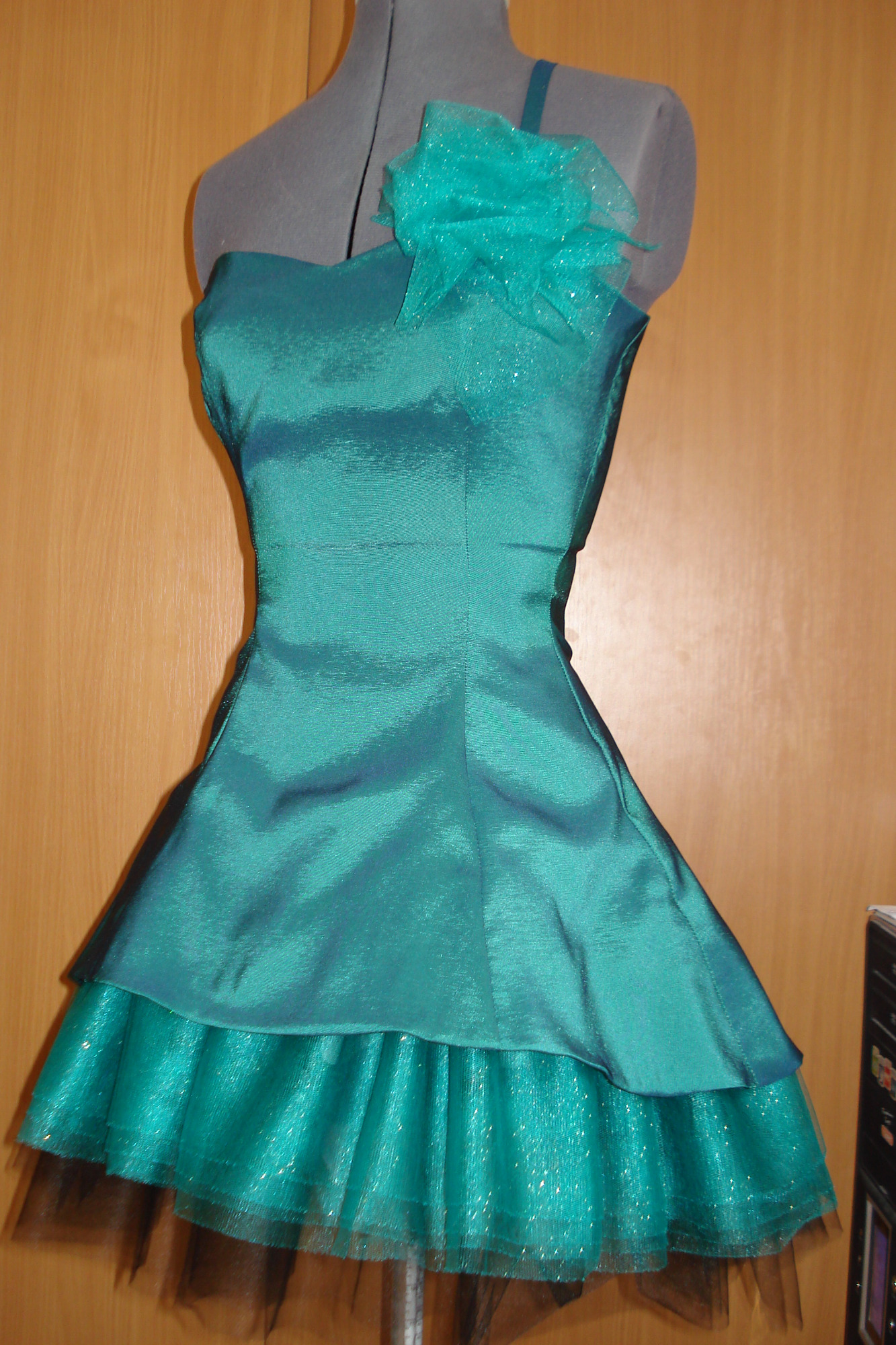 Turkusowa sukienka z tiulowym dołem i ozdobną kokardą na manekinie krawieckim.