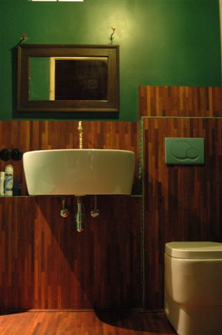 Nowoczesna łazienka z zielonymi ścianami, drewnianą okładziną, wiszącą umywalką i lustrem z dekoracyjnymi ptaszkami.