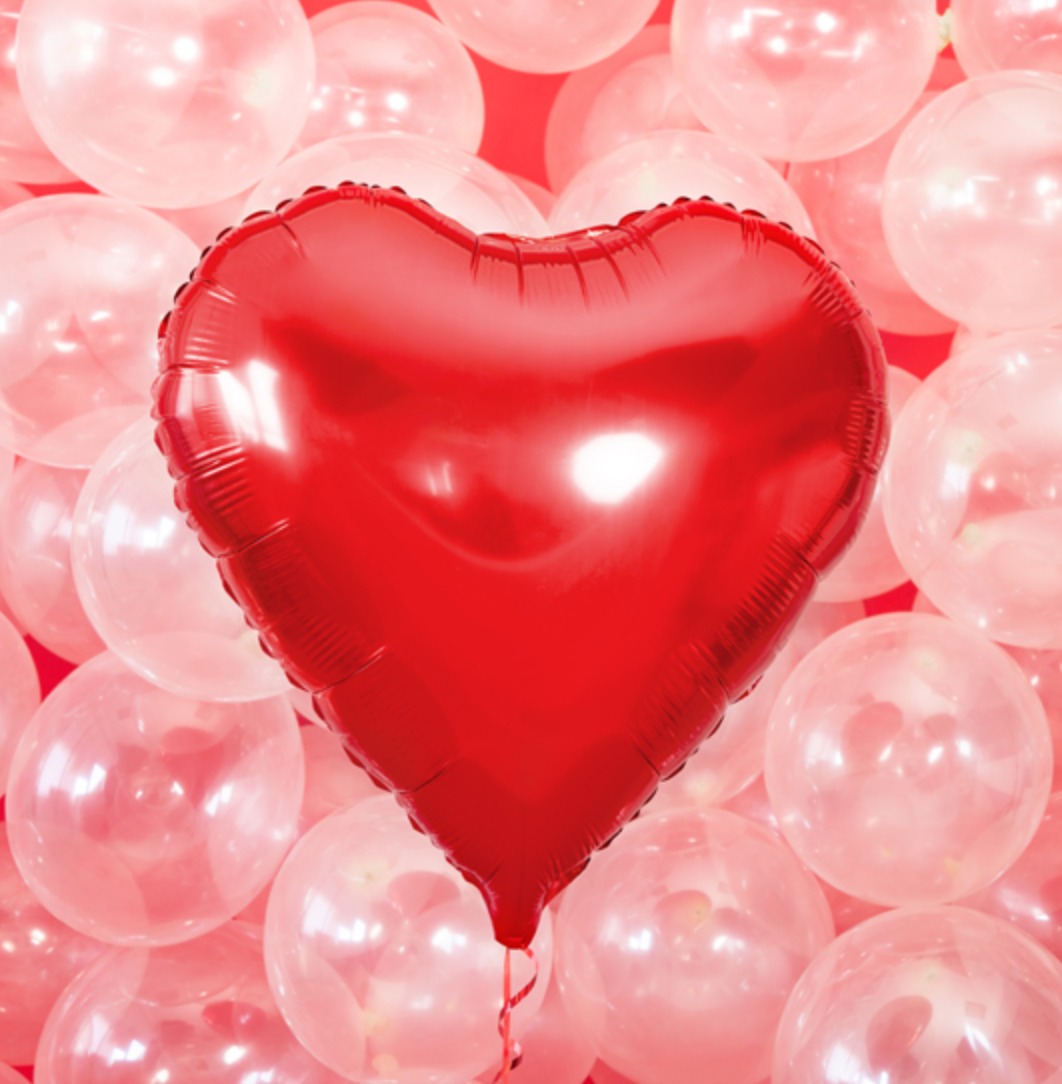 Czerwony, foliowy balon w kształcie serca na tle pastelowych, przezroczystych balonów wypełnionych powietrzem.