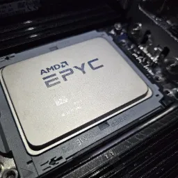 Zamknięte ujęcie procesora AMD EPYC w gnieździe płyty głównej, z widocznymi slotami pamięci RAM i detalami montażu. Oświetlenie podkreśla teksturę komponentów.