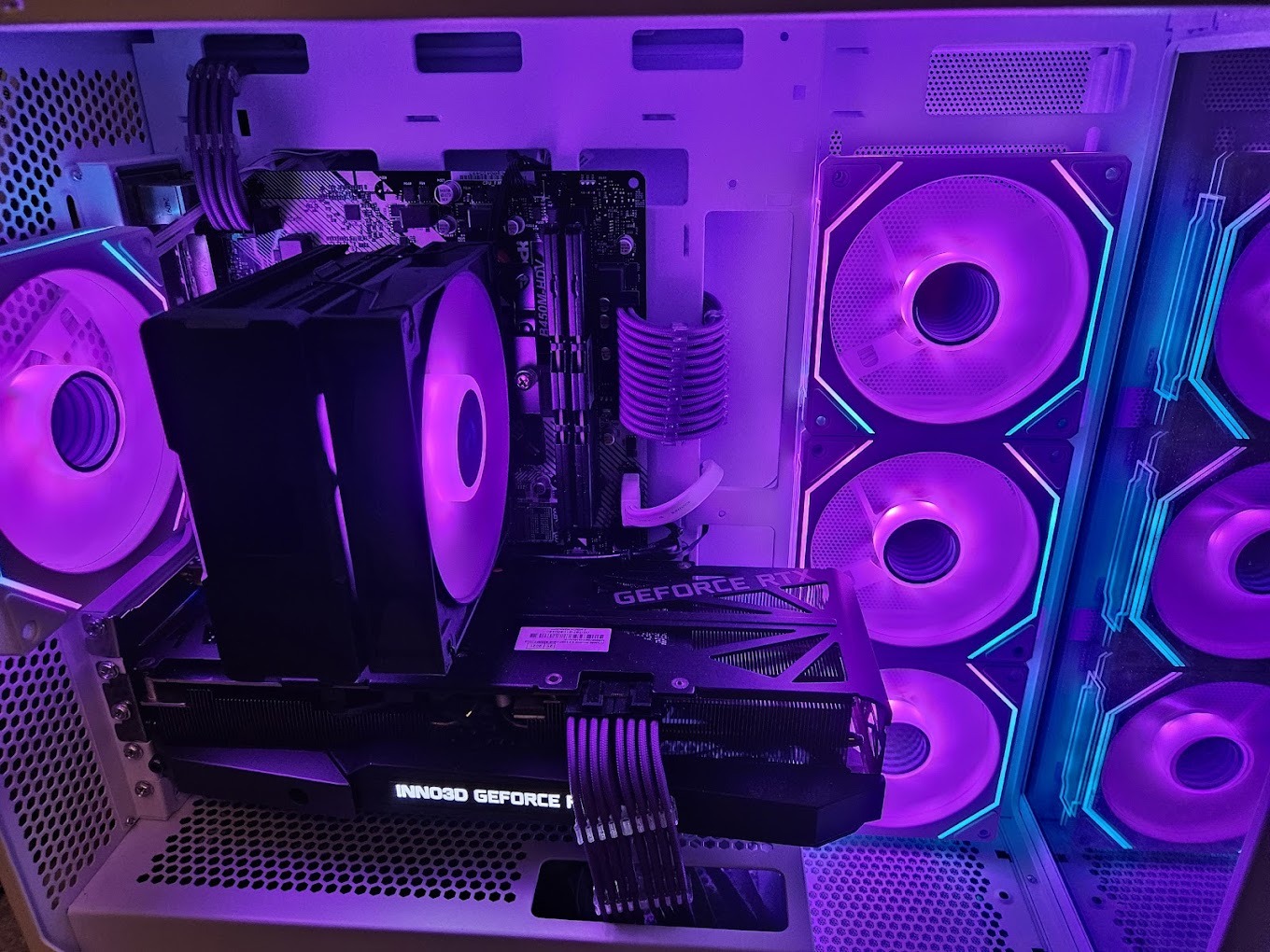 Wnętrze białej obudowy komputera PC z widoczną kartą graficzną INNO3D GeForce RTX, chłodzeniem procesora i podświetlanymi wentylatorami w kolorach fioletu i turkusu.