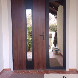 Remofleks Mateusz Ranachowski - Nowoczesne drzwi wejściowe z drewnianym panelem i przeszkleniem, widok z zewnątrz na wejście do domu z widocznym fragmentem ogrodu i elementami wyposażenia.