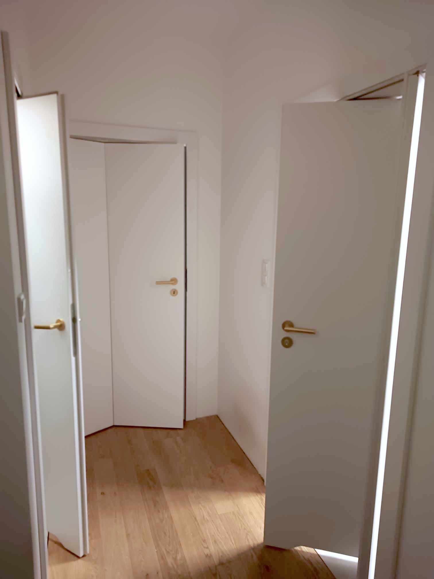 Dwa białe skrzydła drzwiowe z mosiężnymi klamkami, jedno otwarte na oścież, drugie uchylone, widoczne na tle parkietu.