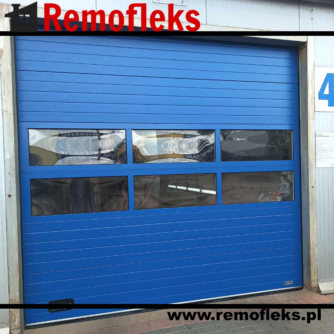Niebieska segmentowa brama garażowa z poziomymi panelami i prostokątnymi oknami, widoczne odbicia w szybach, zewnętrzna instalacja.