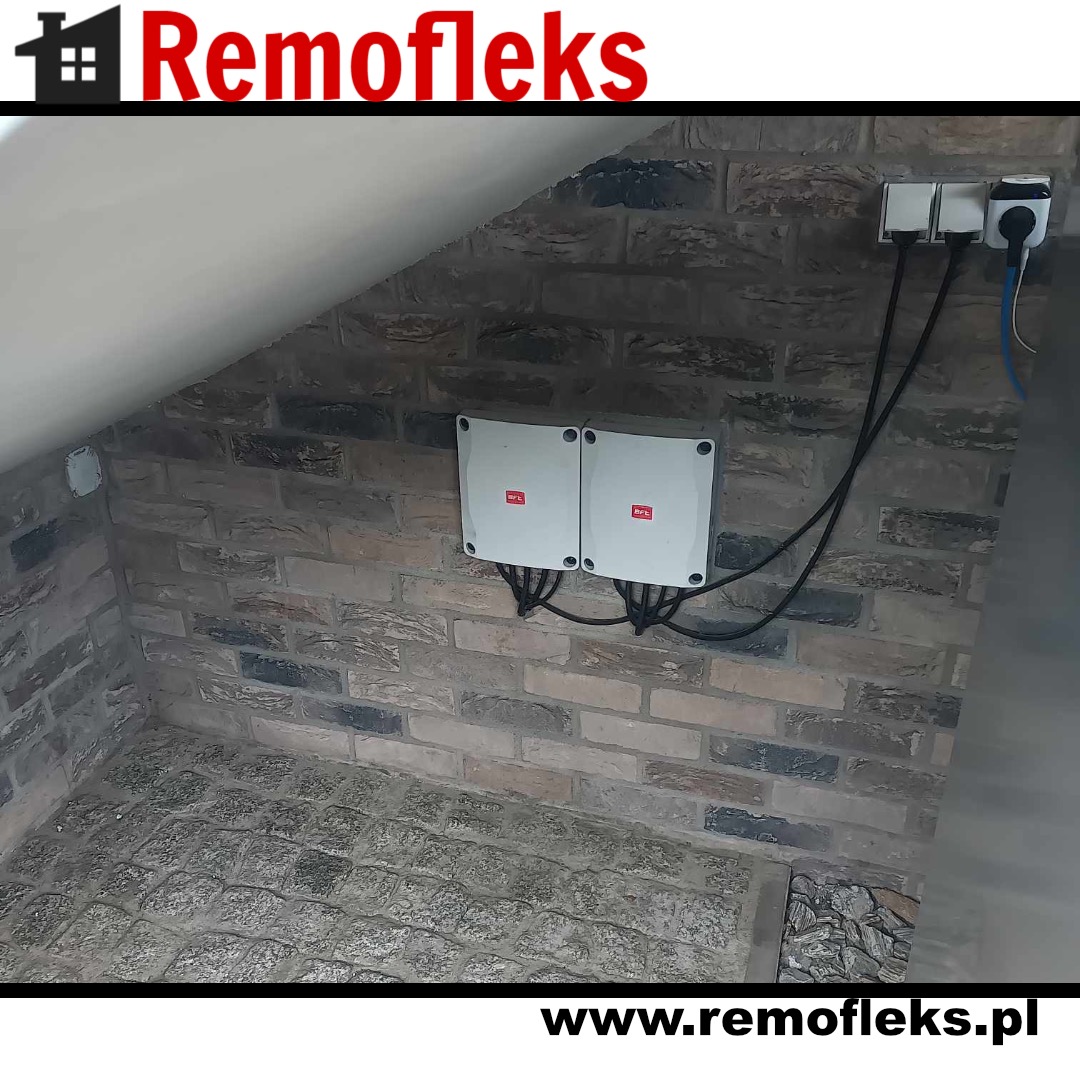 Dwa białe moduły sterujące z logiem BFT zamontowane na ceglanej ścianie pod skosem, z widocznymi kablami i gniazdkami elektrycznymi.