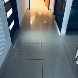 Błyszcząca, jasna podłoga z płytek w korytarzu, widok na otwarte drzwi do innych pomieszczeń, tablica kredowa z napisem po prawej stronie.